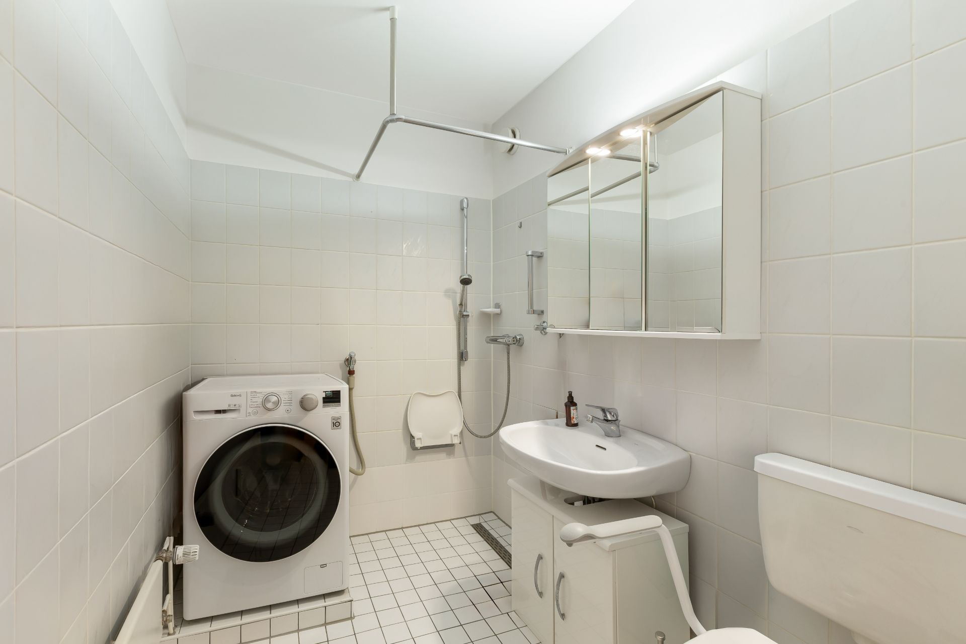 Barrierefreies Badezimmer mit Waschmaschine, Dusche, Waschbecken und Toilette.