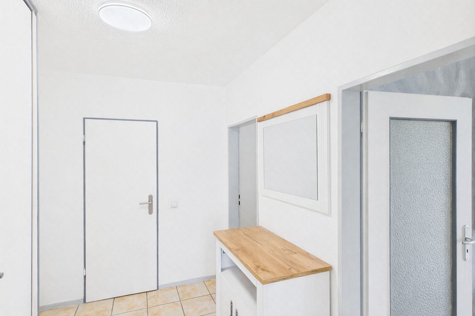 Heller Flur mit Fliesenboden, Holzmöbel und zwei Türen.