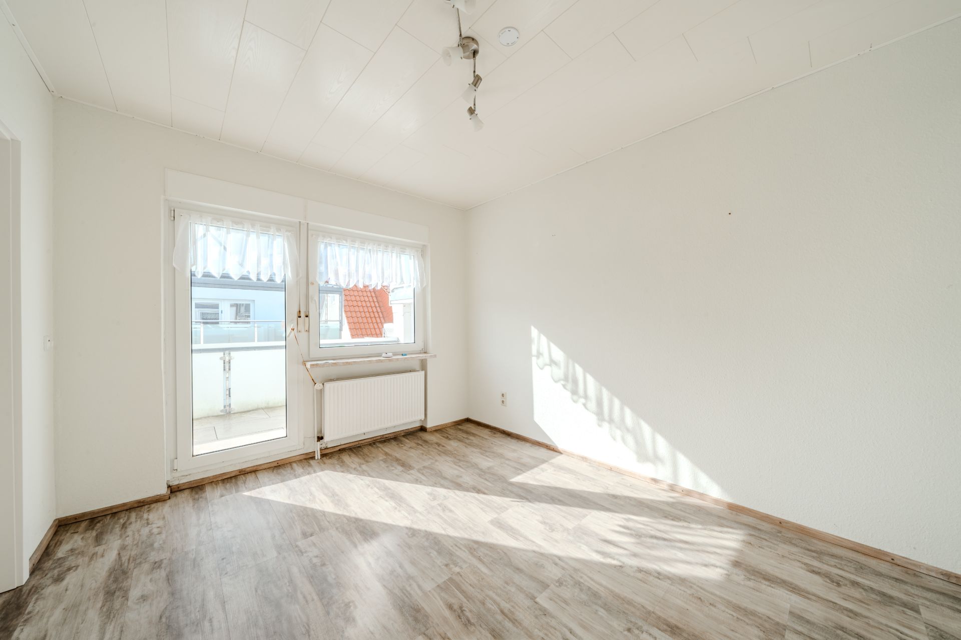 Heller leerer Raum mit großen Fenstern und Boden in Holzoptik.