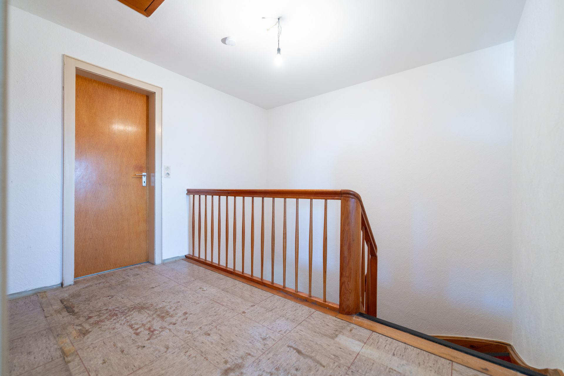 Heller Flur mit Holztür, Holzgeländer und Treppe nach unten.