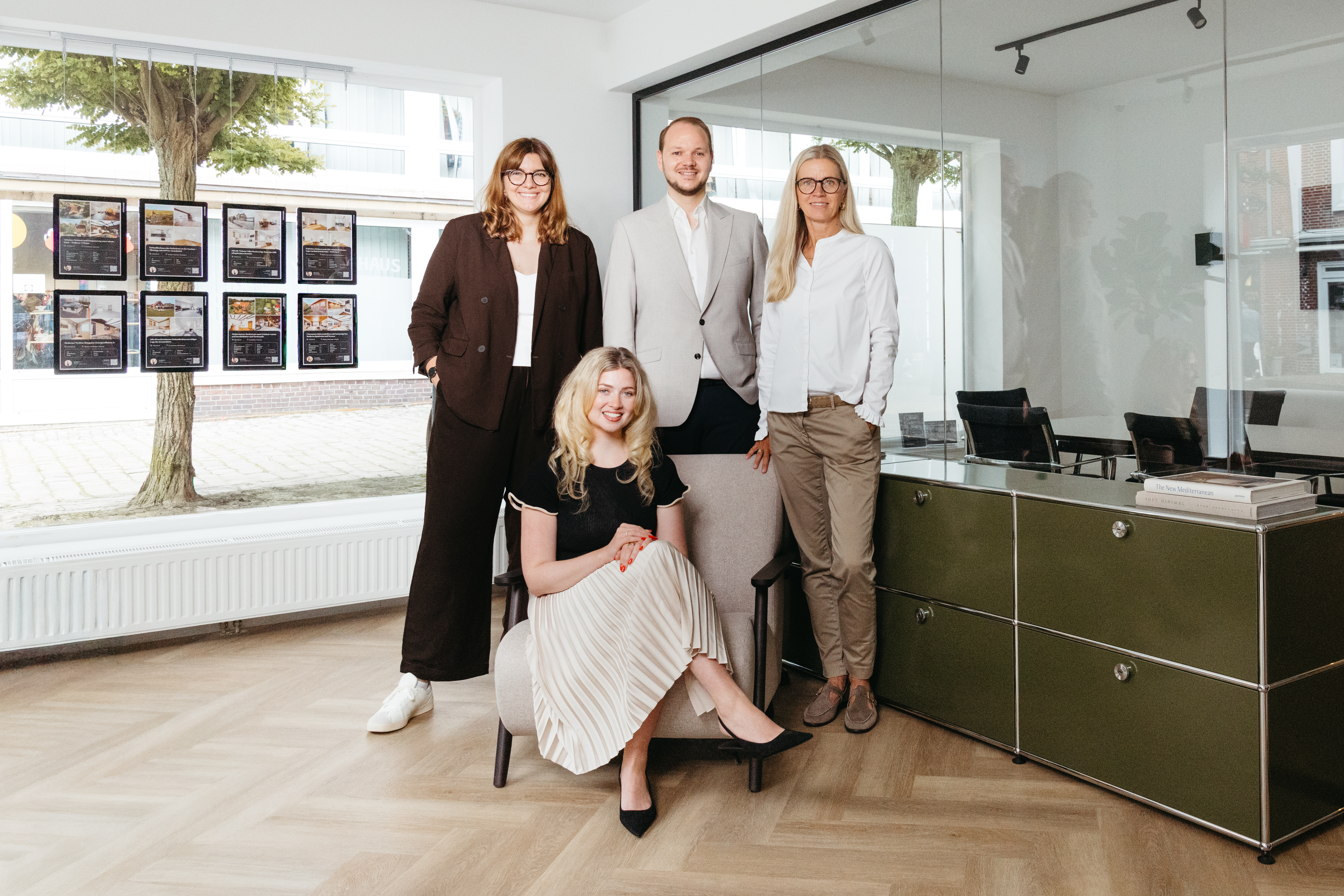 Vier Personen posieren in einem modernen Büro mit großen Fenstern und Büromöbeln.
