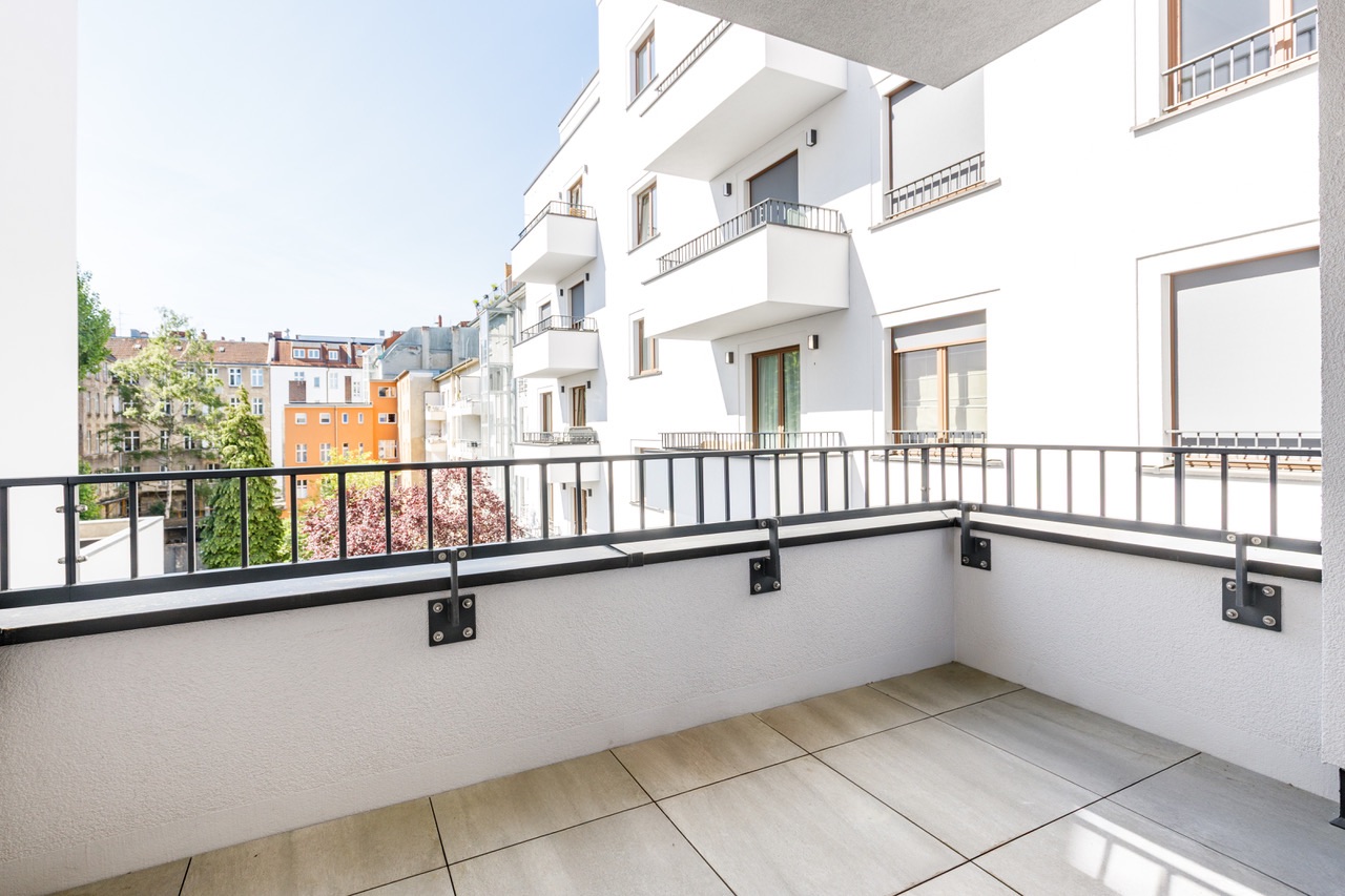 Moderner Balkon mit Fliesenboden und Blick auf benachbarte Wohngebäude bei Tageslicht.