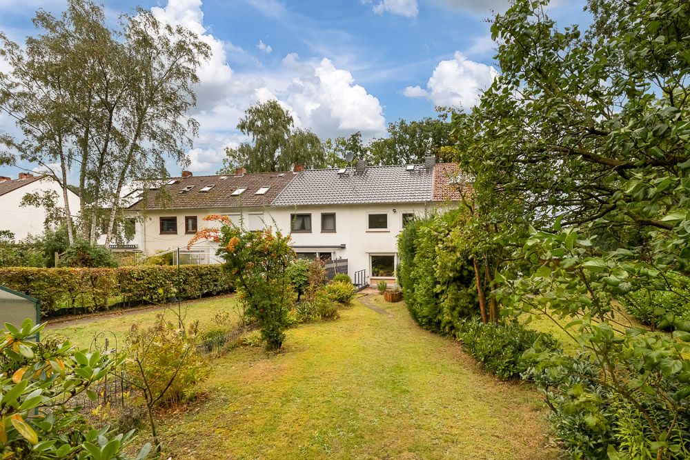 Reihenhaus mit großem Garten, umgeben von Bäumen und Sträuchern bei Tageslicht.