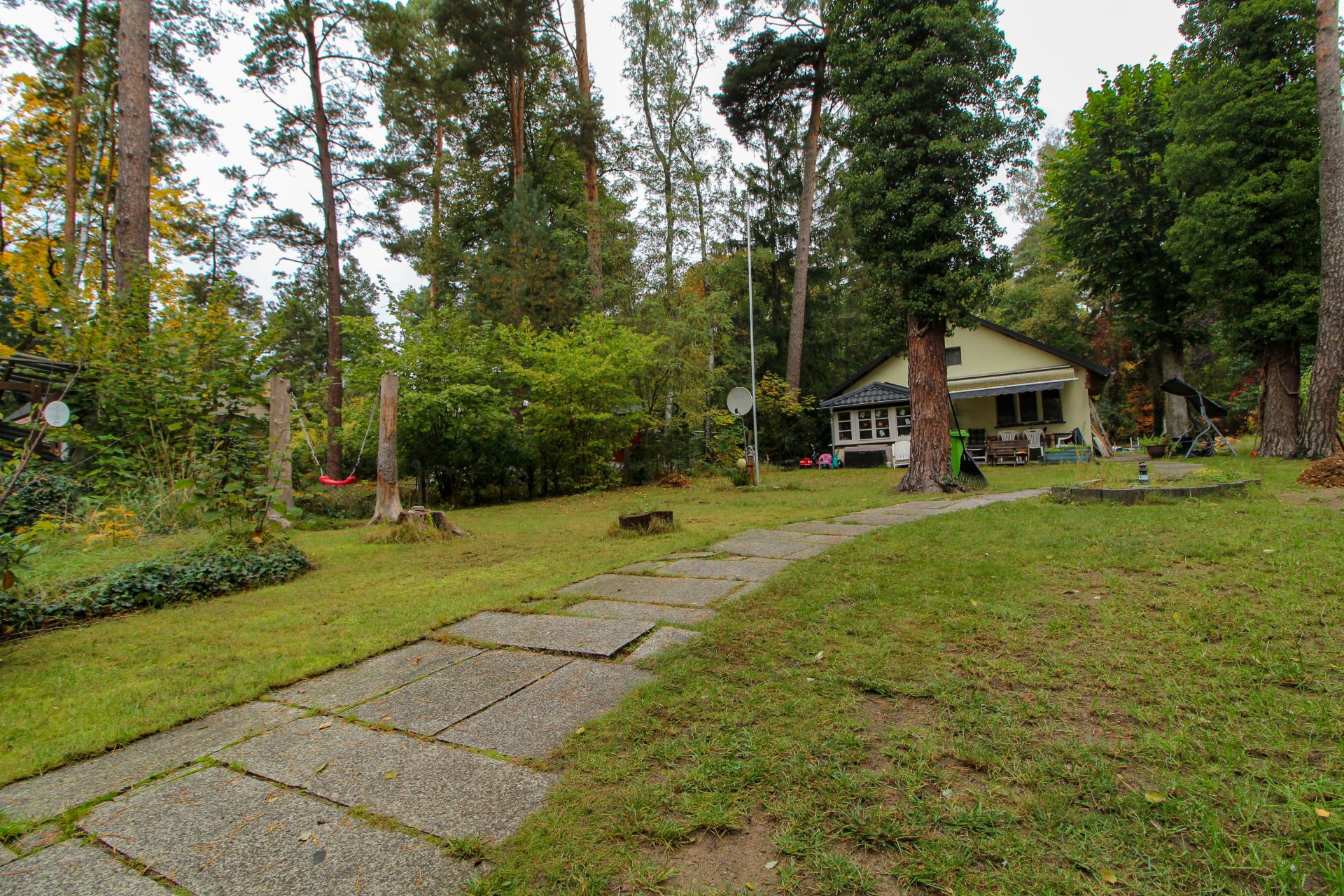 Garten mit Steinweg, Bäumen und kleinem Haus im Hintergrund.