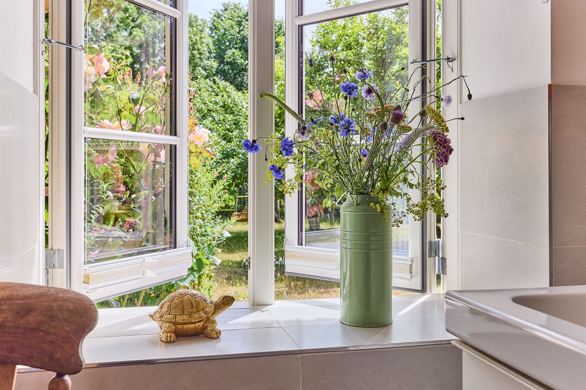 Offenes Fenster mit Blumenstrauß in Vase und goldener Schildkröte auf der Fensterbank.