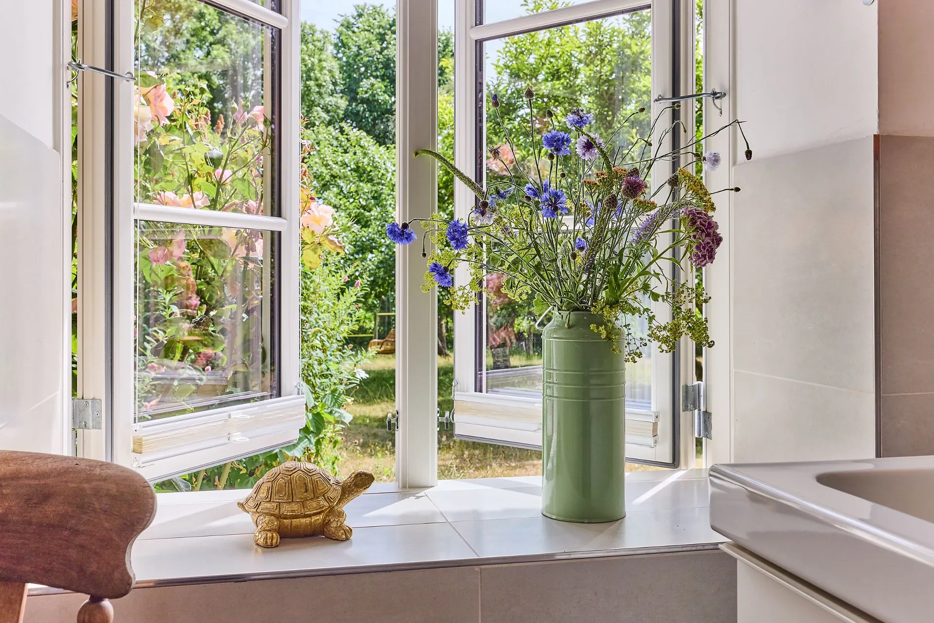 Offenes Fenster mit Blumenstrauß in Vase und goldener Schildkröte auf der Fensterbank.
