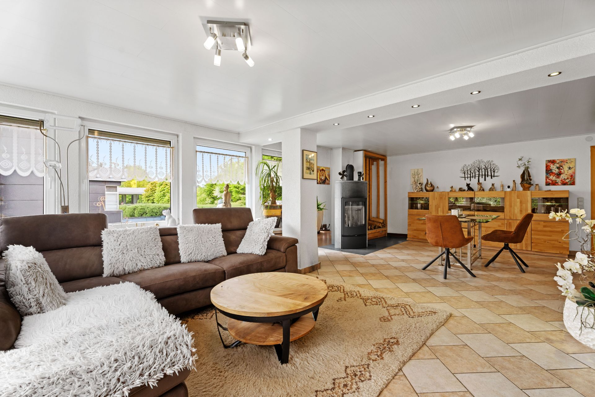 Helles Wohnzimmer mit braunem Sofa, rundem Holztisch und Essbereich im Hintergrund.