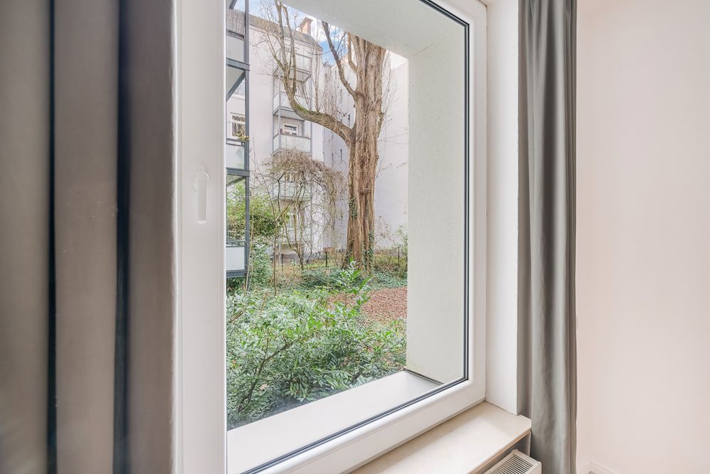 Blick aus einem Fenster auf einen begrünten Innenhof mit Bäumen und Sträuchern.