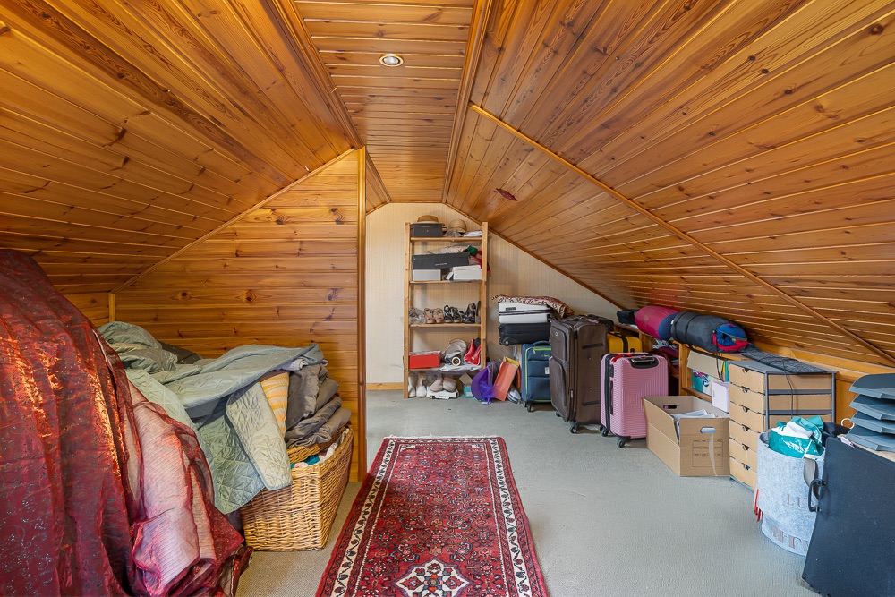 Abstellraum mit Holzdecke, Regalen, Kisten und Koffern unterm Dach.