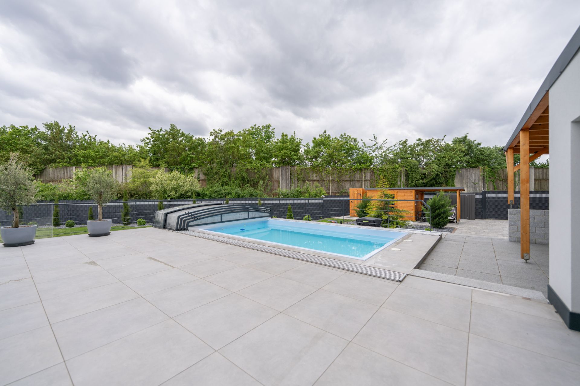 Moderner Garten mit Pool, großen Fliesen und einigen Pflanzen am Rand.
