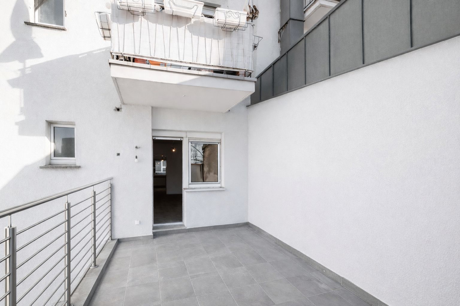 Große, geflieste Terrasse mit Metallgeländer und Zugang zu einer Wohnung.