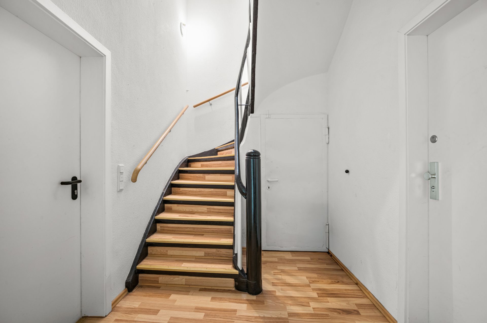 Heller Flur mit Holztreppe, zwei weißen Türen und Parkettboden.