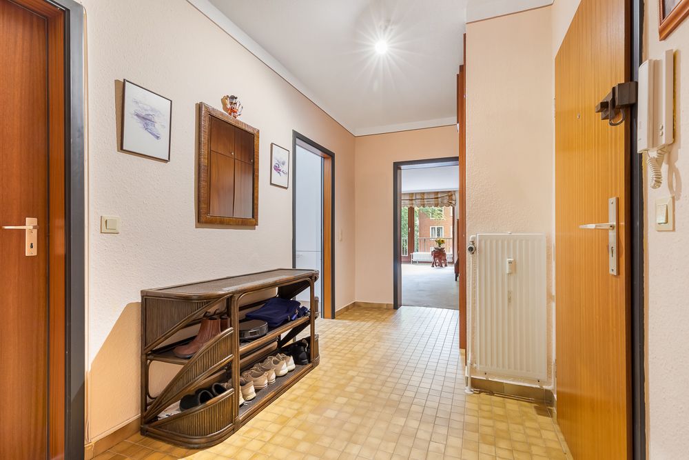 Heller Flur mit Schuhregal, Spiegel und Bildern an der Wand, Türen zu weiteren Räumen sichtbar.
