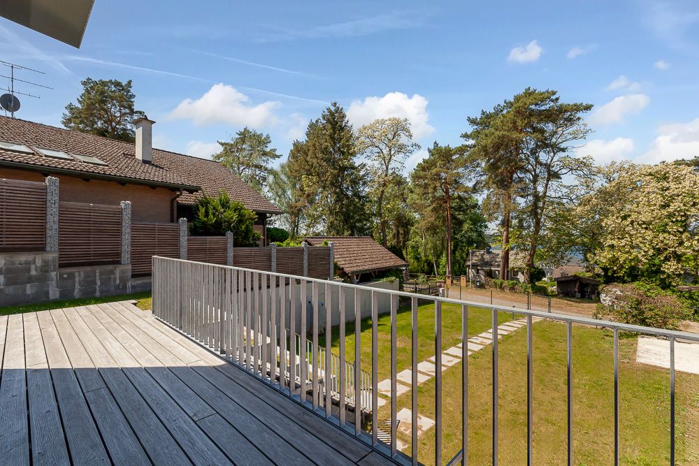 Blick von einem Holzbalkon auf einen Garten mit Rasen, Bäumen und Gartenweg.