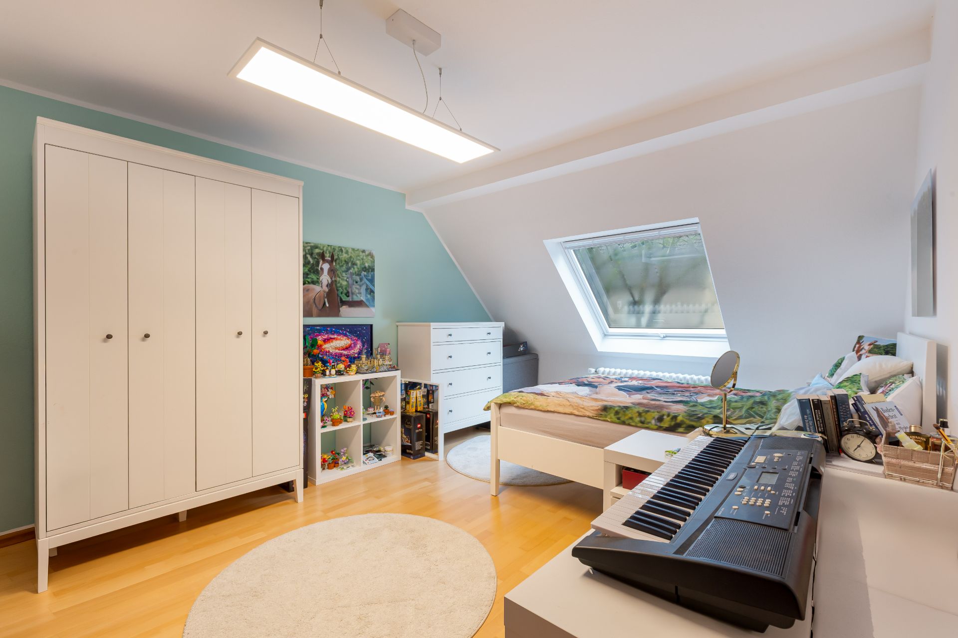 Helles Kinderzimmer mit Bett, Kleiderschrank, Schreibtisch, Regal, Keyboard und großem Fenster.