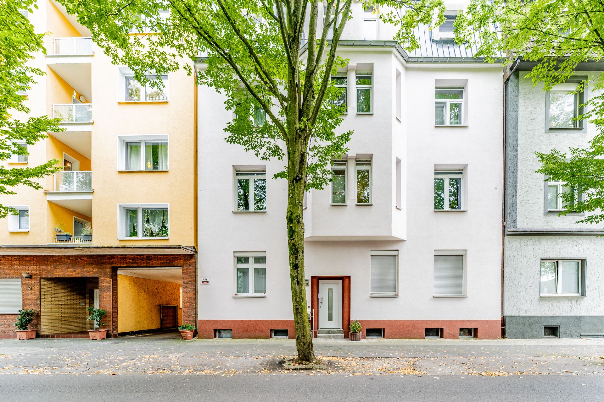 Fassade eines mehrstöckigen Wohnhauses mit weißer Wand und Baum davor.