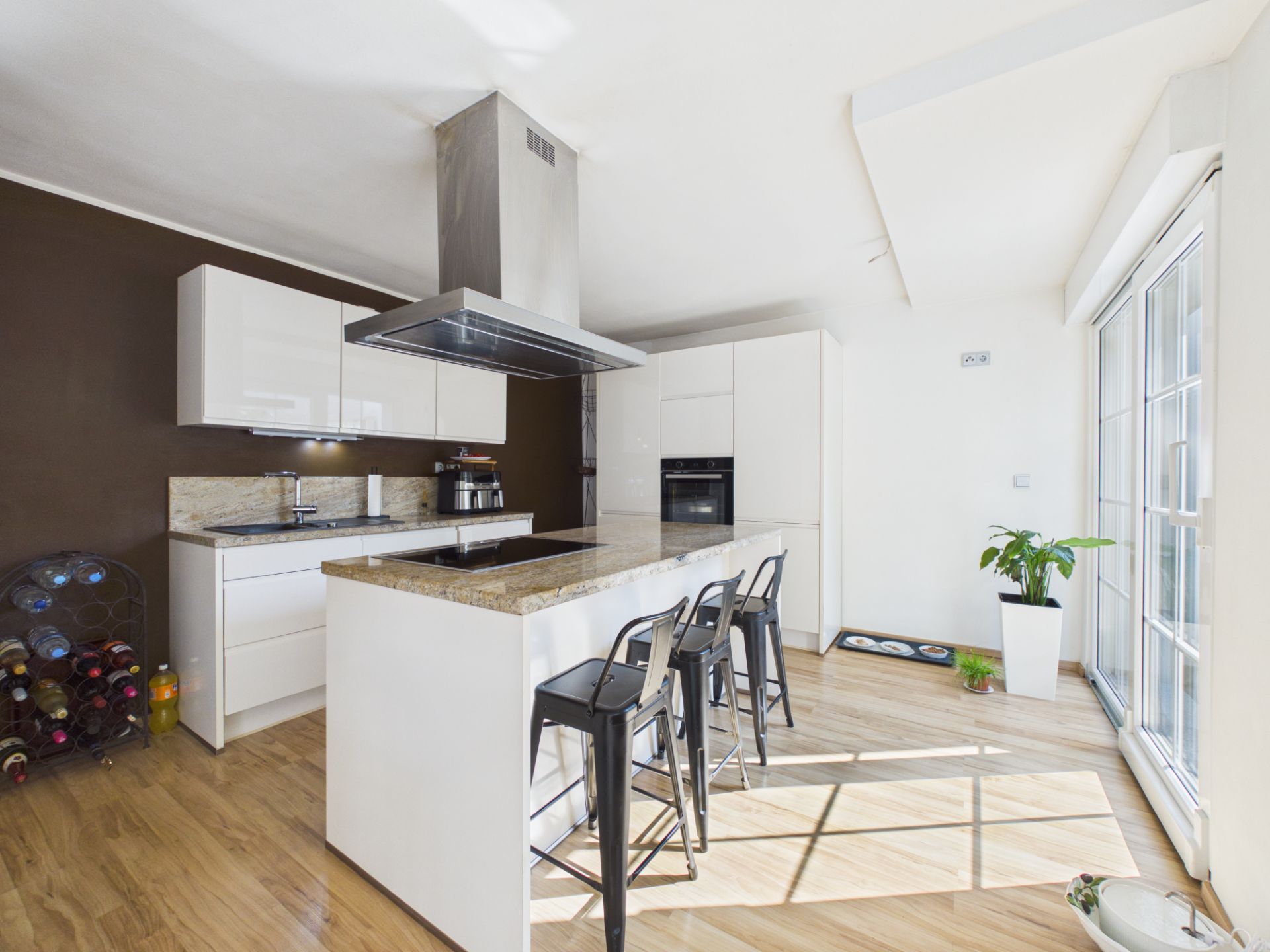 Moderne Küche mit Kücheninsel, drei Stühlen, großem Fenster und Holzboden.