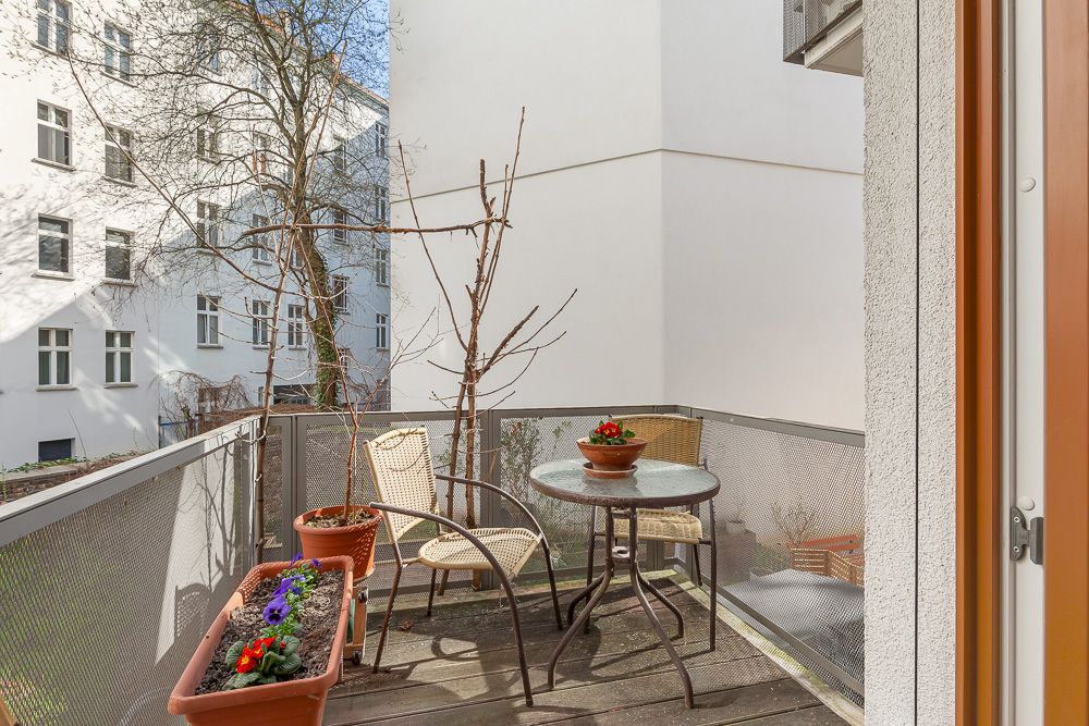 Kleiner Balkon mit zwei Stühlen, rundem Glastisch und Blumenkästen an einem Wohngebäude.