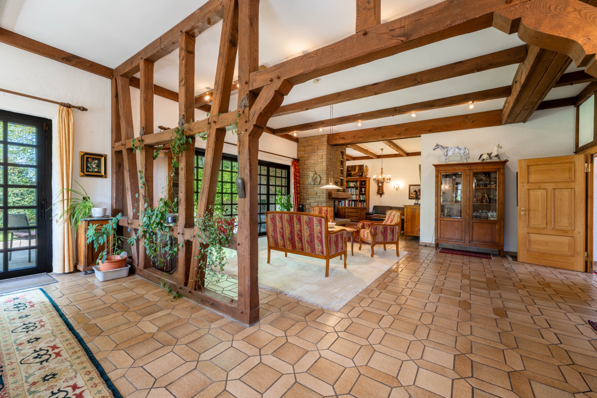 Helles Wohnzimmer mit Holzbalken, Sitzbereich, Fliesenboden und vielen Pflanzen.