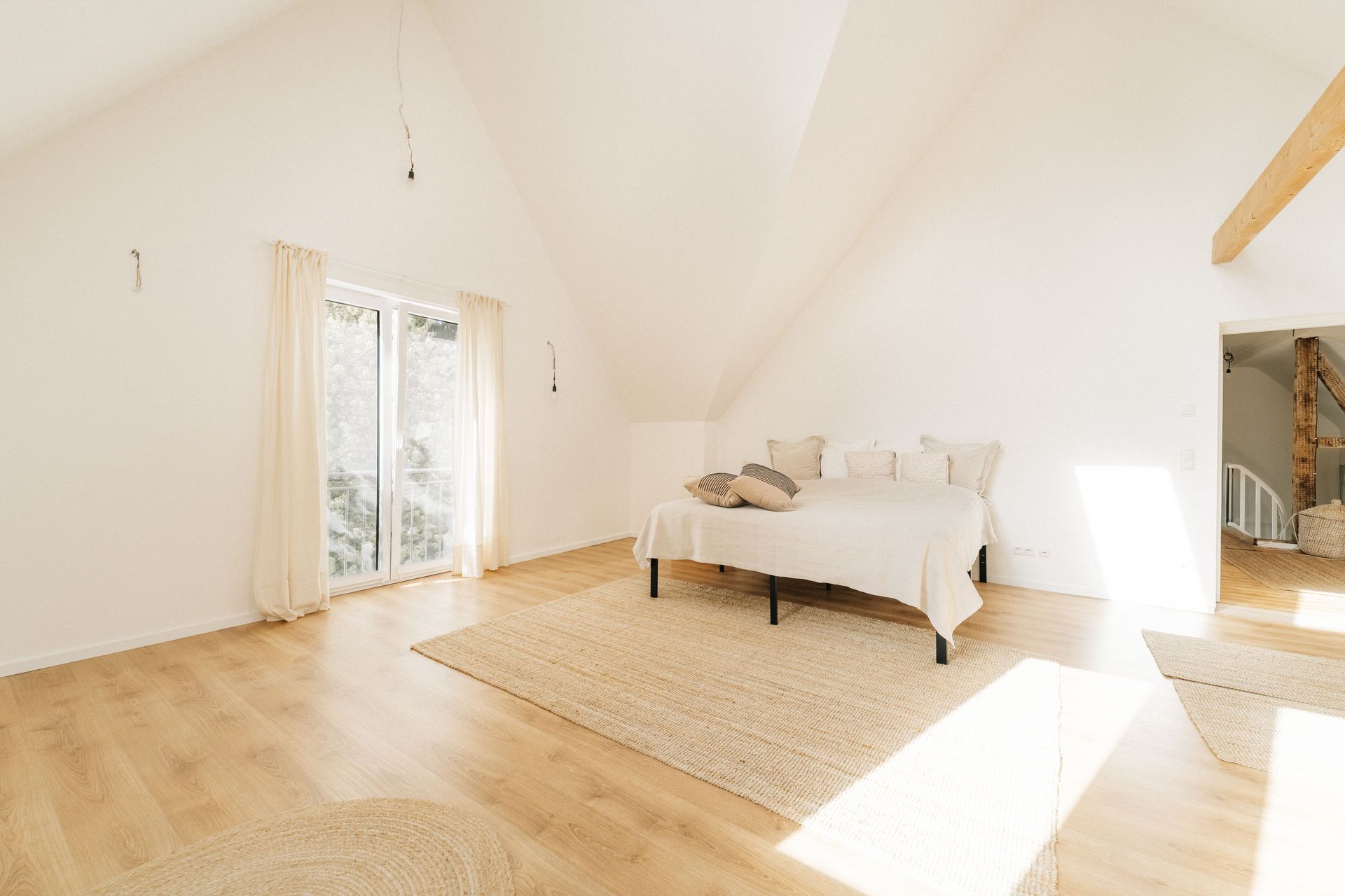 Helles Schlafzimmer mit Holzboden, großem Bett, Teppichen und bodentiefem Fenster.