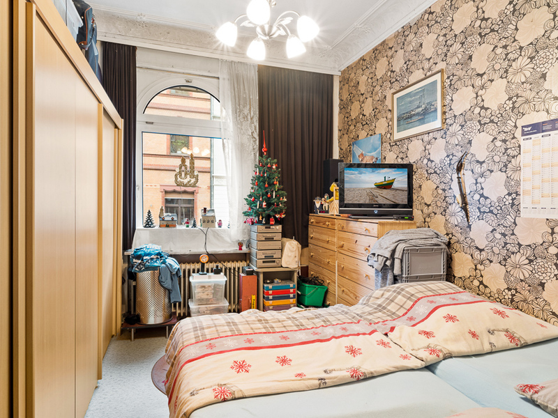 Wohnzimmer mit Doppelbett, Schrank, Kommode, TV, Fenster und kleinem Weihnachtsbaum.