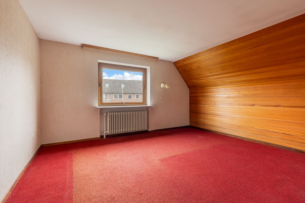 Leerer Raum mit rotem Teppich, Holzvertäfelung an einer Wand und Fenster mit Heizkörper.