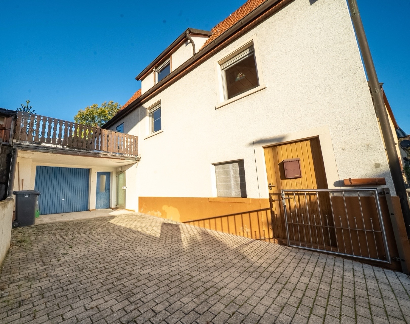Hof mit gepflastertem Boden, Haus mit brauner Tür, blauer Garage und Balkon.