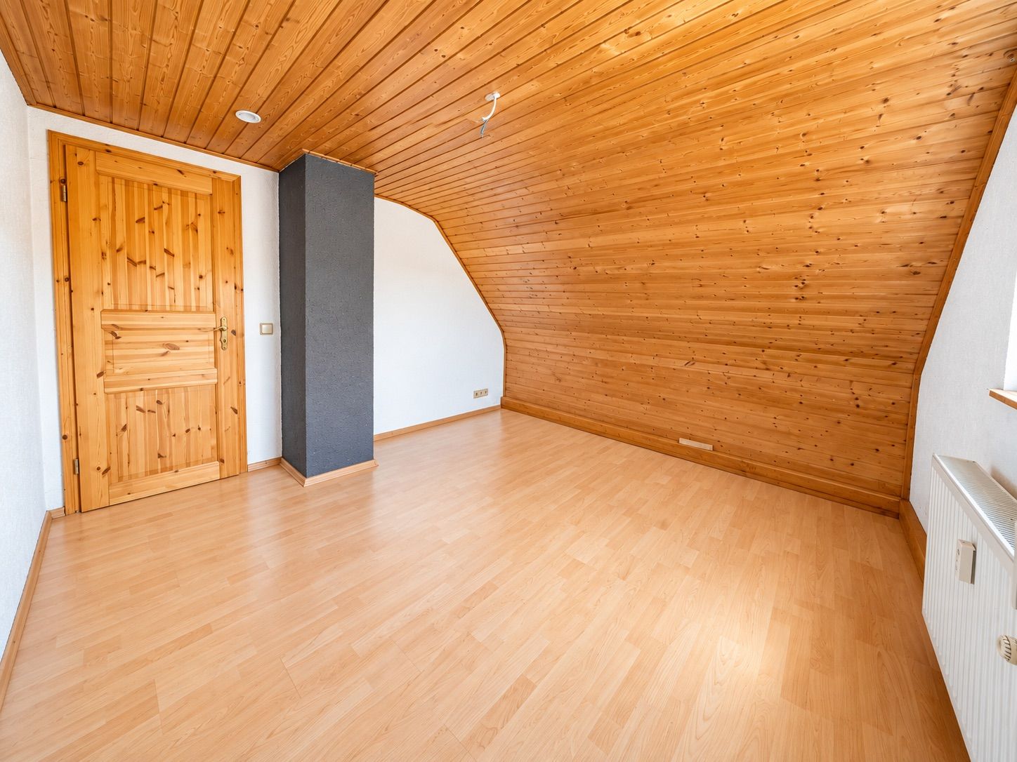 Leerstehendes Zimmer mit Holzdecke, Holztür und schräger Wandverkleidung aus Holz.
