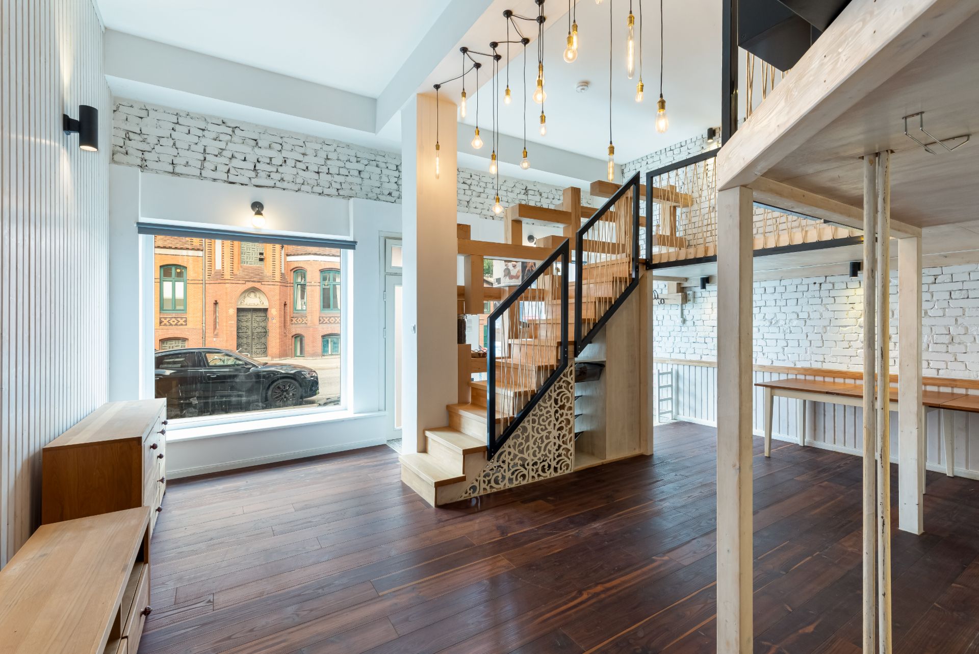 Modernes Wohnzimmer mit Holztreppe, großen Fenstern und weißen Backsteinwänden.