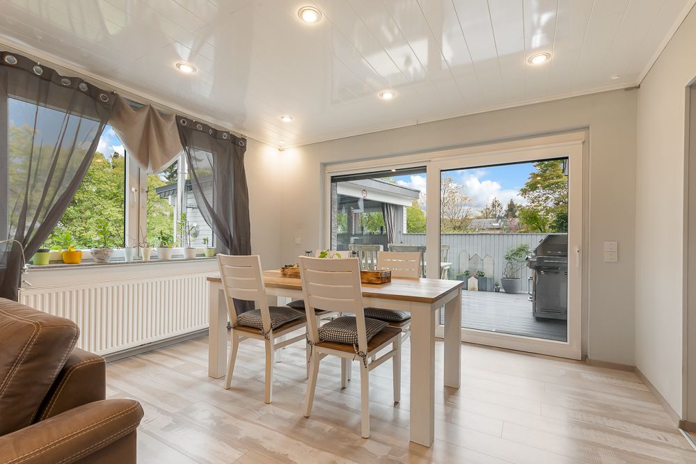 Essbereich mit Holztisch und vier Stühlen, große Fenster und Zugang zur Terrasse mit Grill.