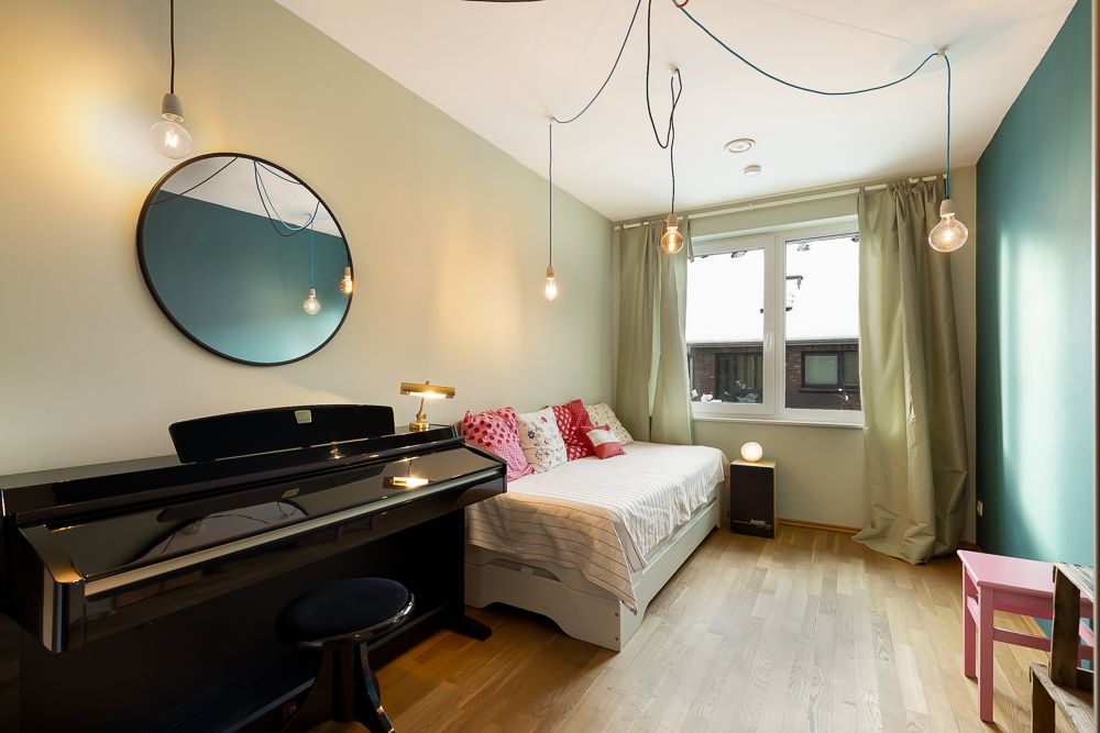 Helles Zimmer mit Klavier, Einzelbett, rundem Spiegel und großen Fenstern mit Vorhängen.