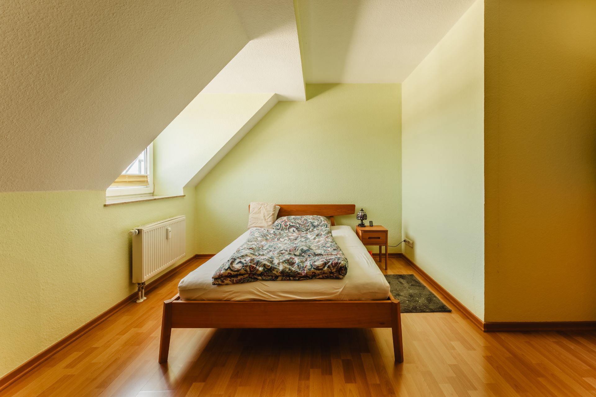 Schlafzimmer mit Einzelbett, Nachttisch und Fenster unter Dachschräge.