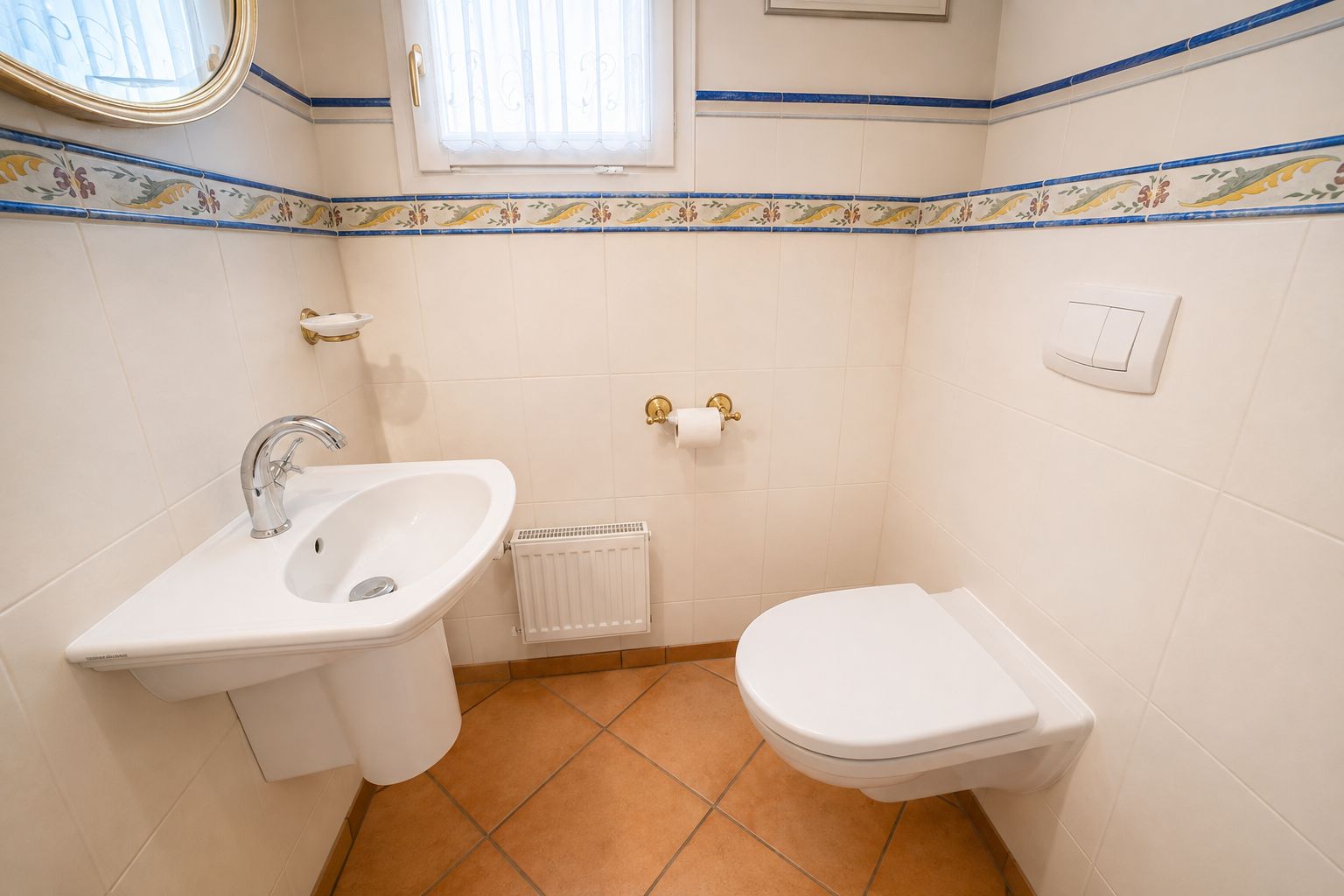 Kleines Badezimmer mit Wandtoilette, Waschbecken, Spiegel, Fenster und Fliesenboden.