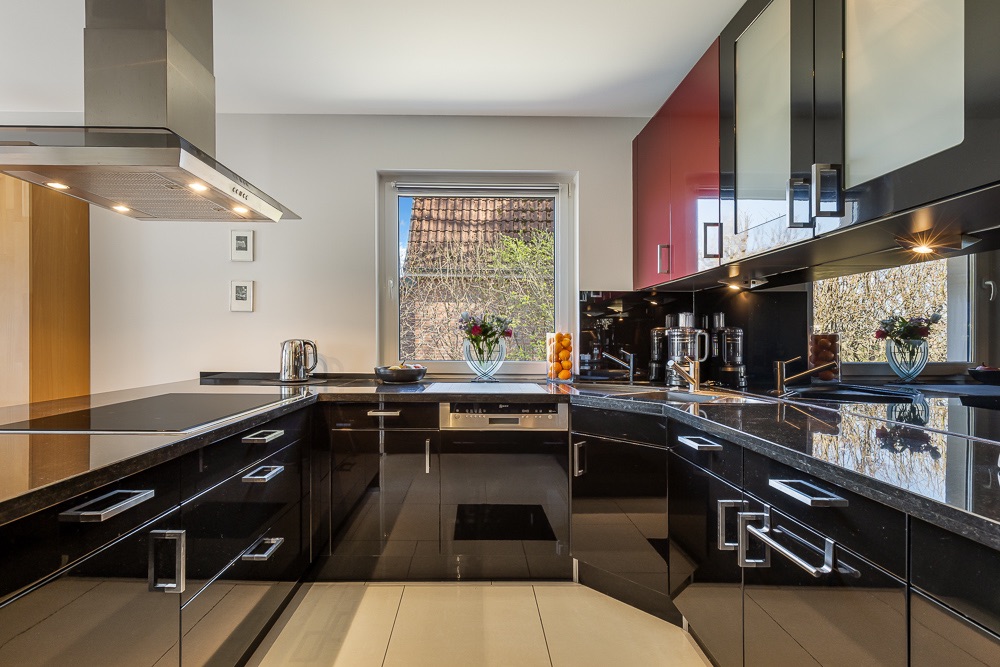 Moderne Küche mit schwarzen Hochglanzschränken und Fenster über der Spüle.