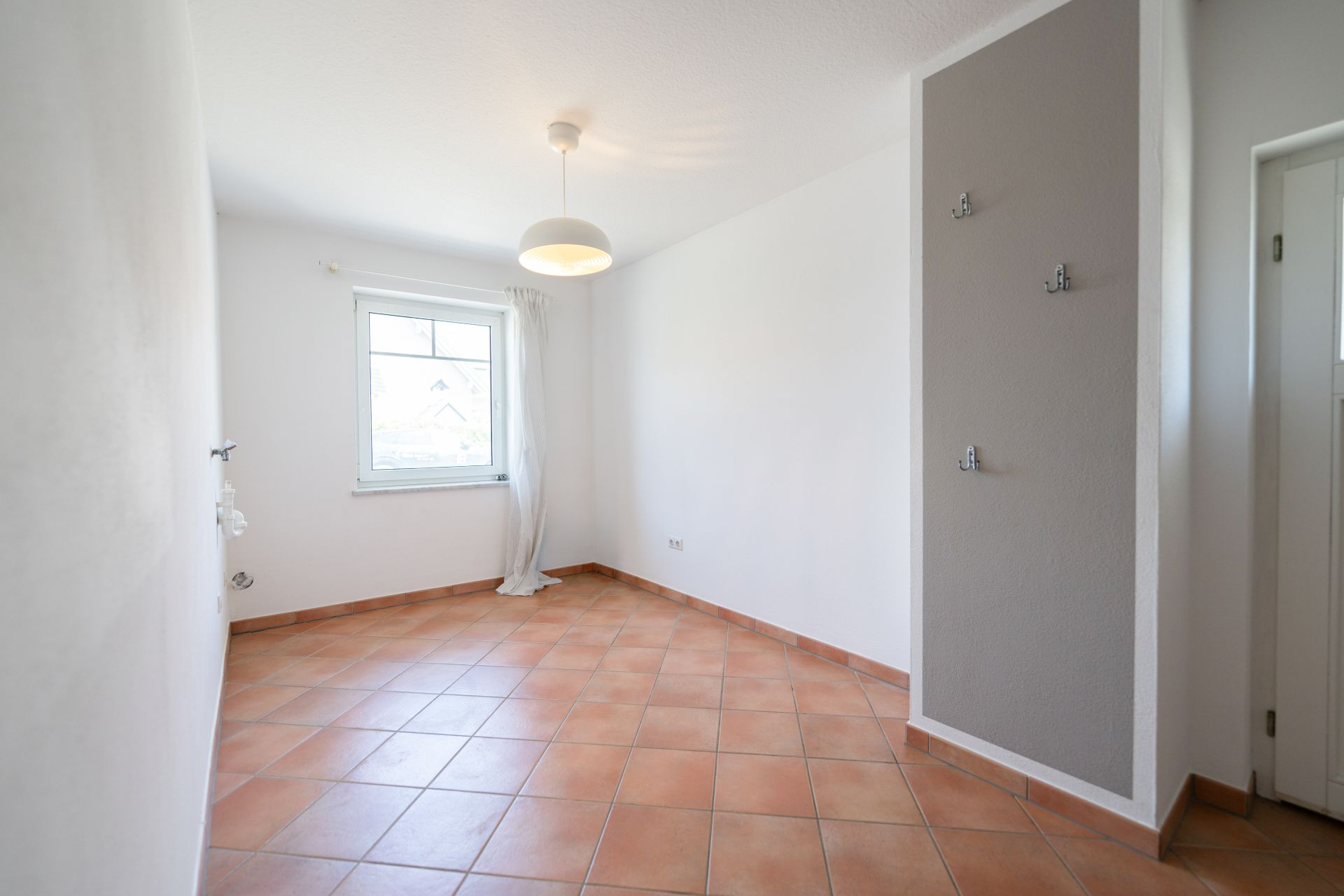 Leeres Zimmer mit Fliesenboden, Fenster, weißer Wand und Deckenlampe.