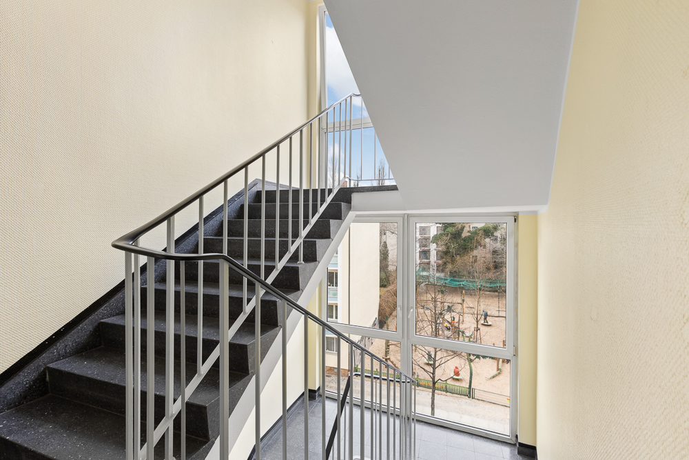 Treppenhaus mit Geländer und großem Fenster mit Blick auf einen Spielplatz.