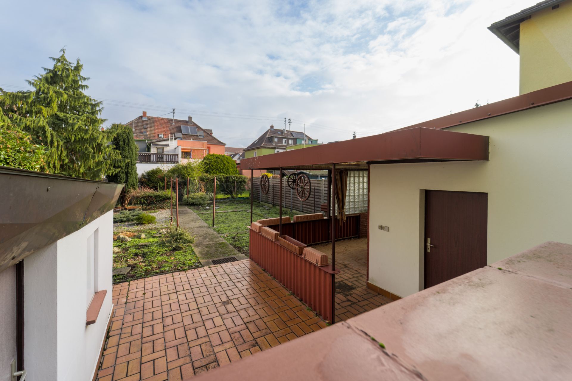Gepflasterte Terrasse mit überdachtem Bereich und Garten im Hintergrund.