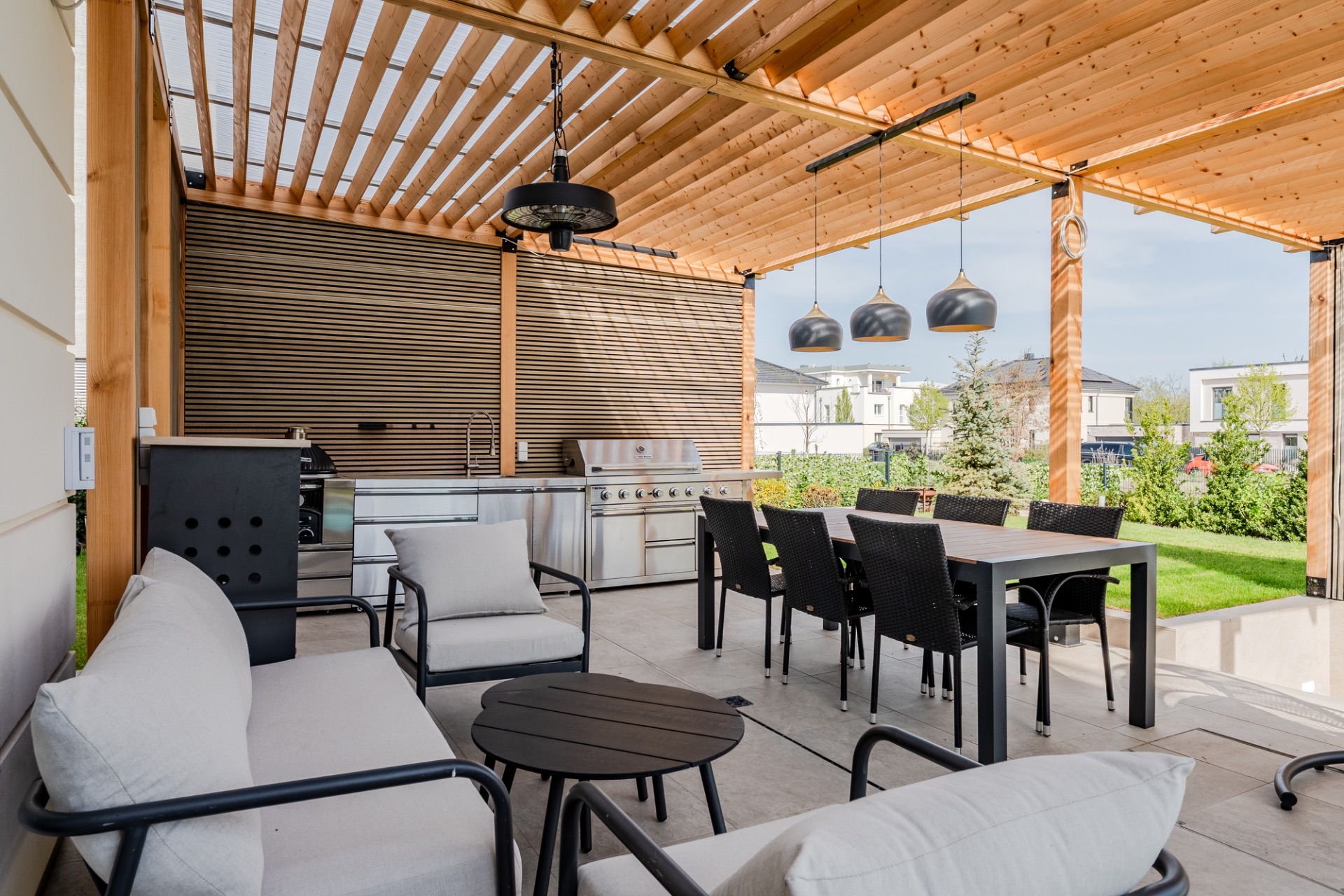 Überdachte Terrasse mit Sitzgruppe, Esstisch, Grill und Gartenblick.