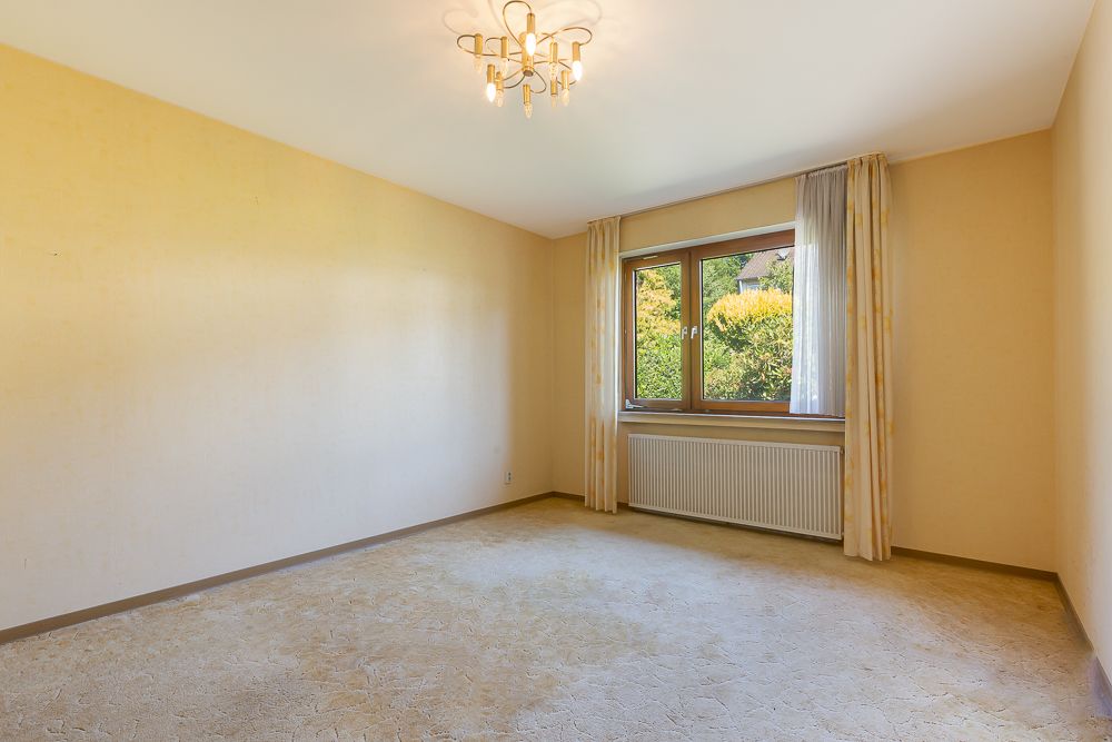 Leerer Raum mit gelben Wänden, großem Fenster, Vorhängen, Teppichboden und Deckenleuchte.