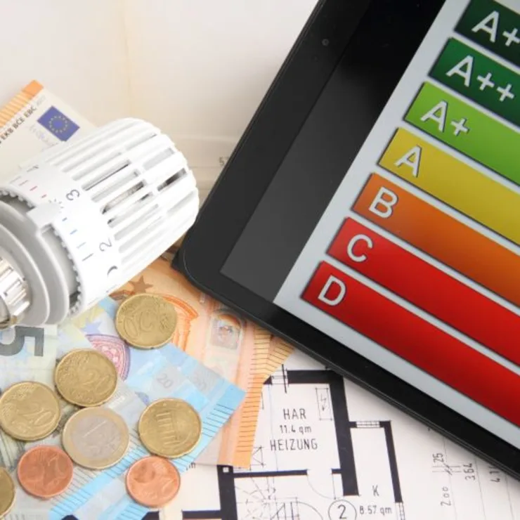 Heizungsregler, Euroscheine und Münzen, Tablet mit Energieeffizienzskala, Ausschnitt eines Grundrisses.