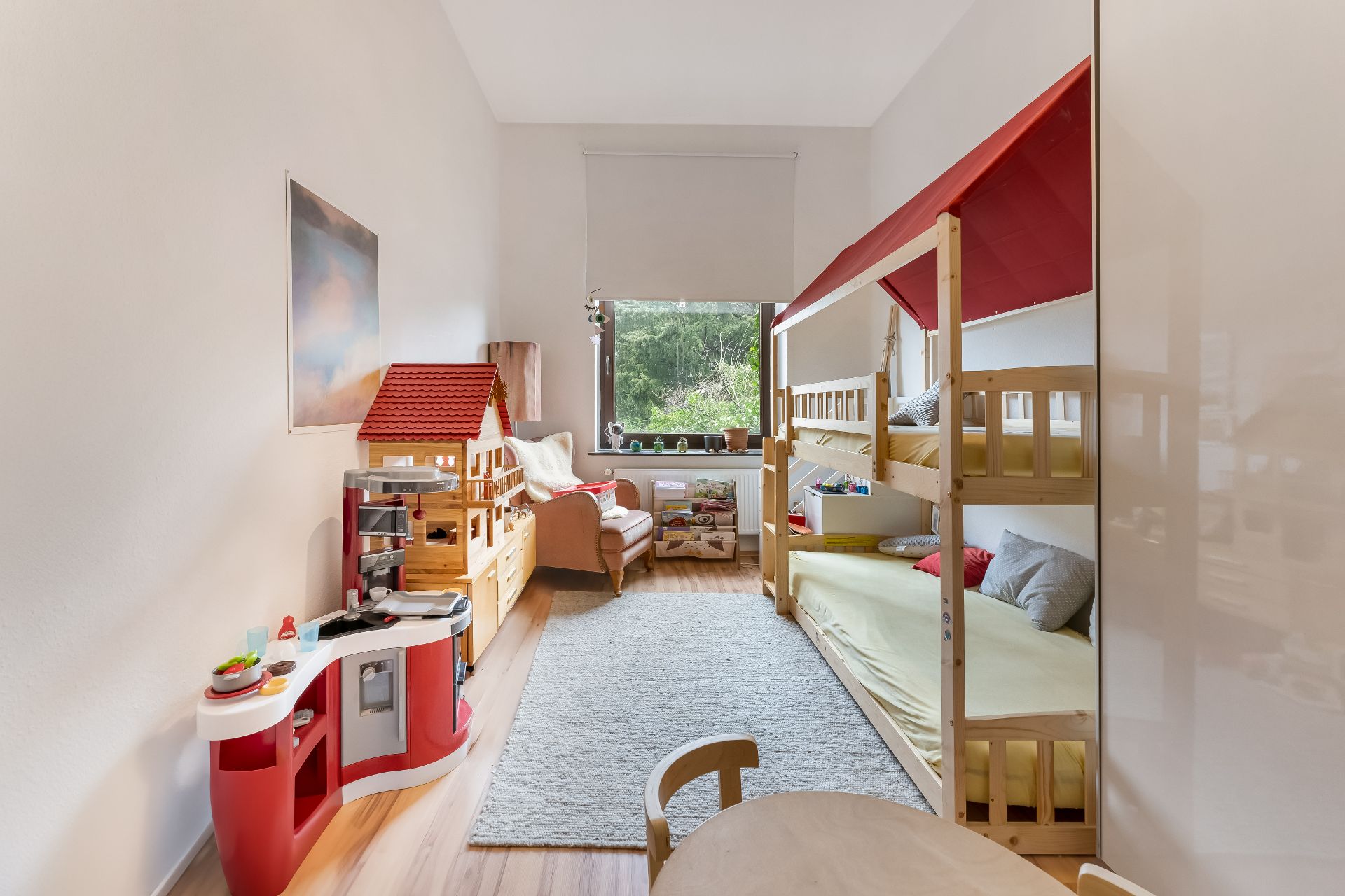 Kinderzimmer mit Etagenbett, Spielküche, Puppenhaus und Fenster mit Blick ins Grüne.