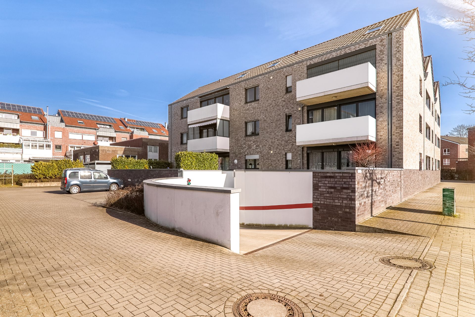 Modernes Wohnhaus mit Balkonen, Garagenzufahrt und geparktem Auto auf gepflastertem Hof.