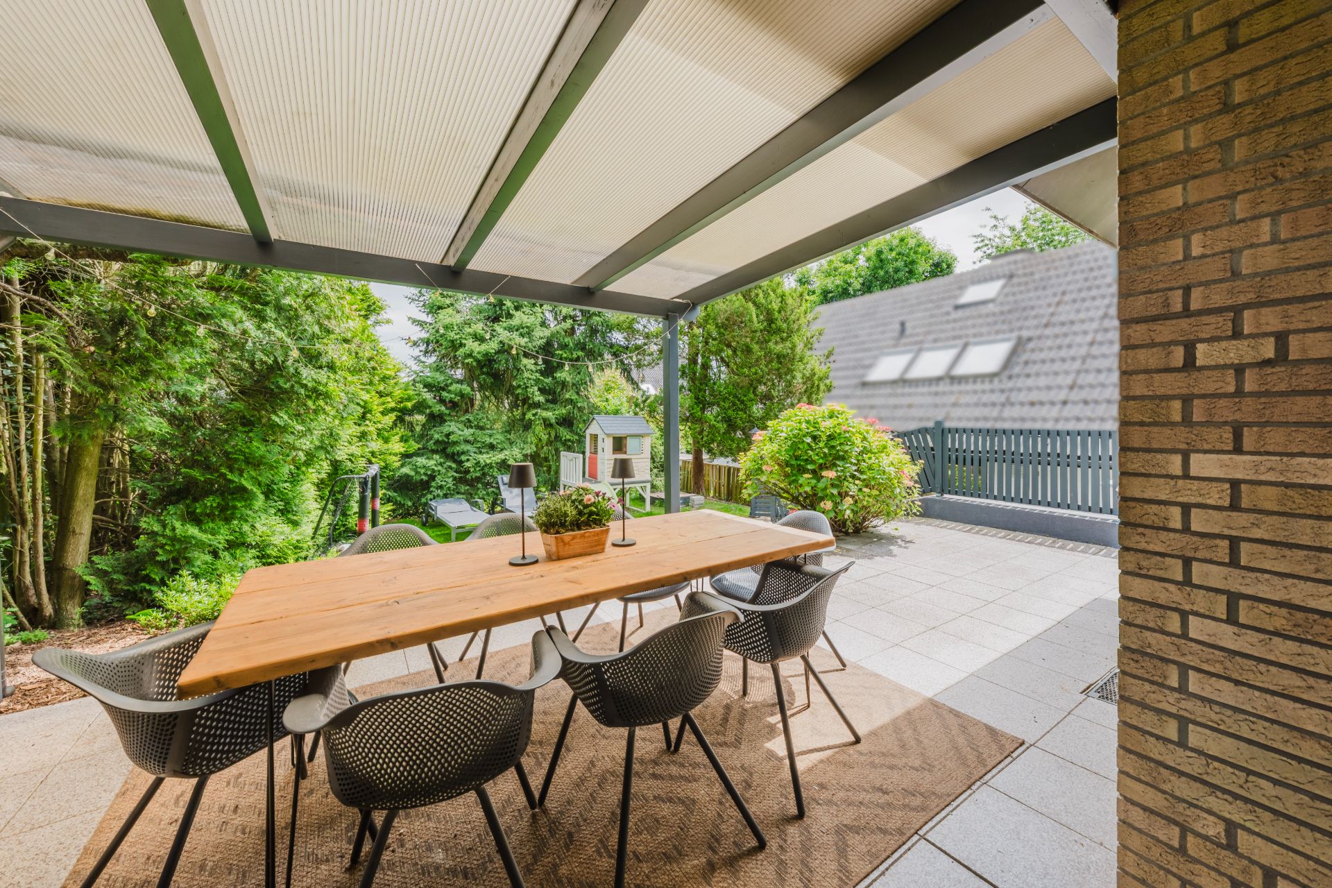 Überdachte Terrasse mit Holztisch, acht Stühlen und Blick in einen grünen Garten.
