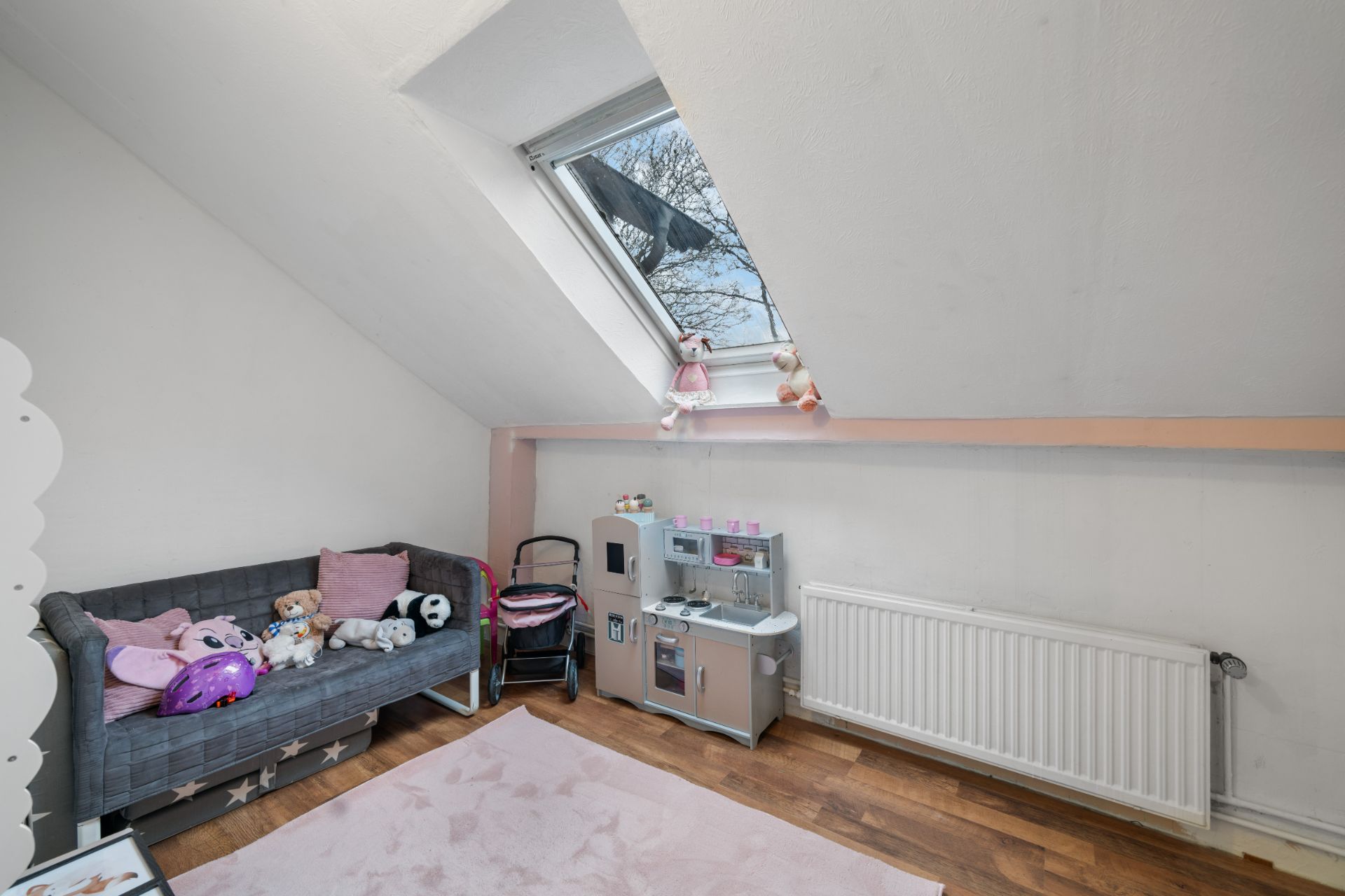 Kinderzimmer mit Spielküche, Sofa mit Stofftieren und Dachfenster.