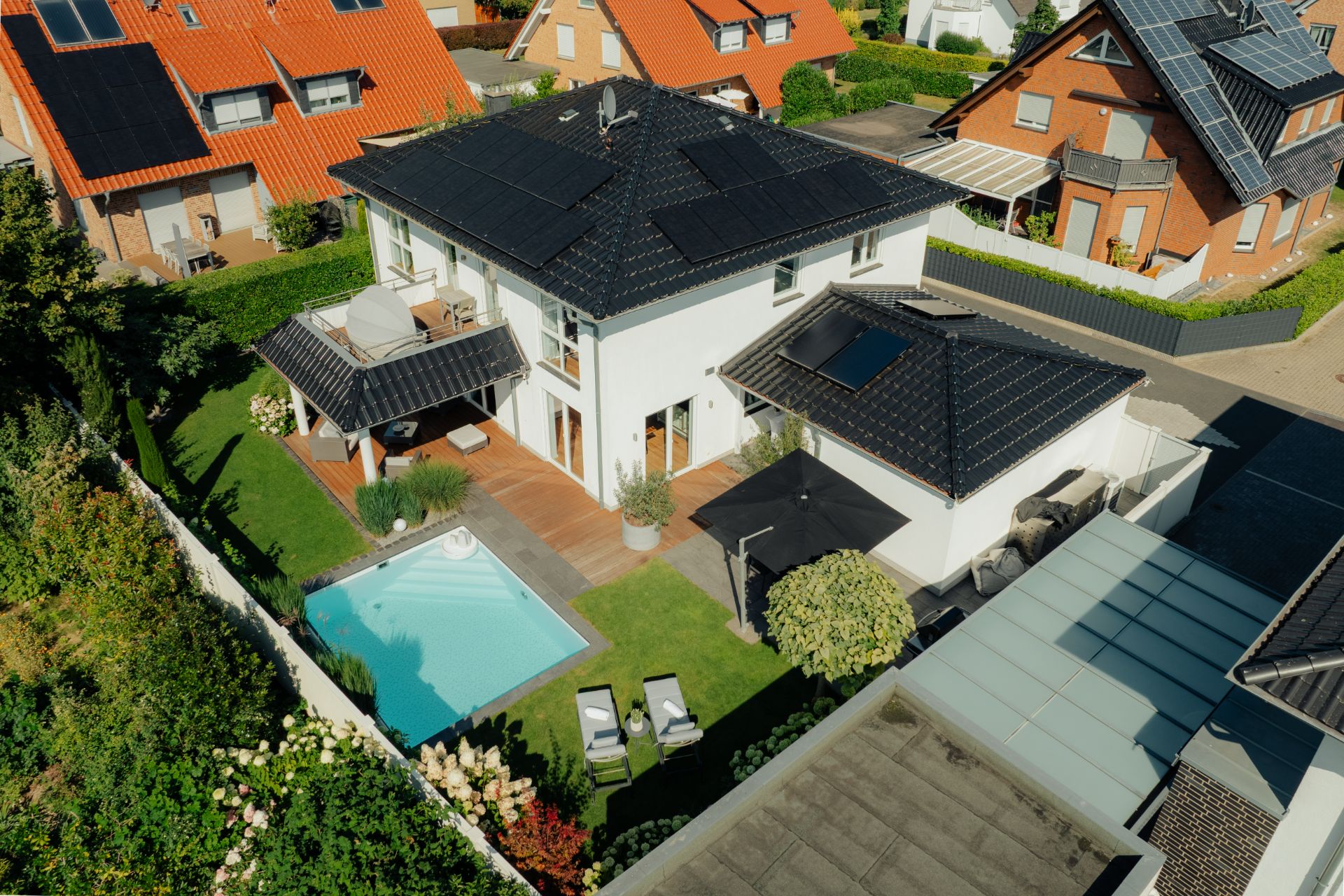 Luftaufnahme eines modernen Einfamilienhauses mit Garten, Pool und Terrasse in Wohngegend.