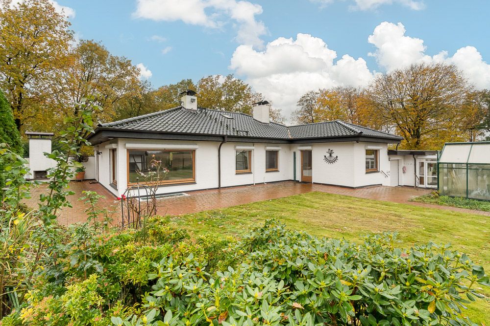 Weiße einstöckige Wohnhaus mit dunklem Dach und großem Garten, umgeben von Bäumen.