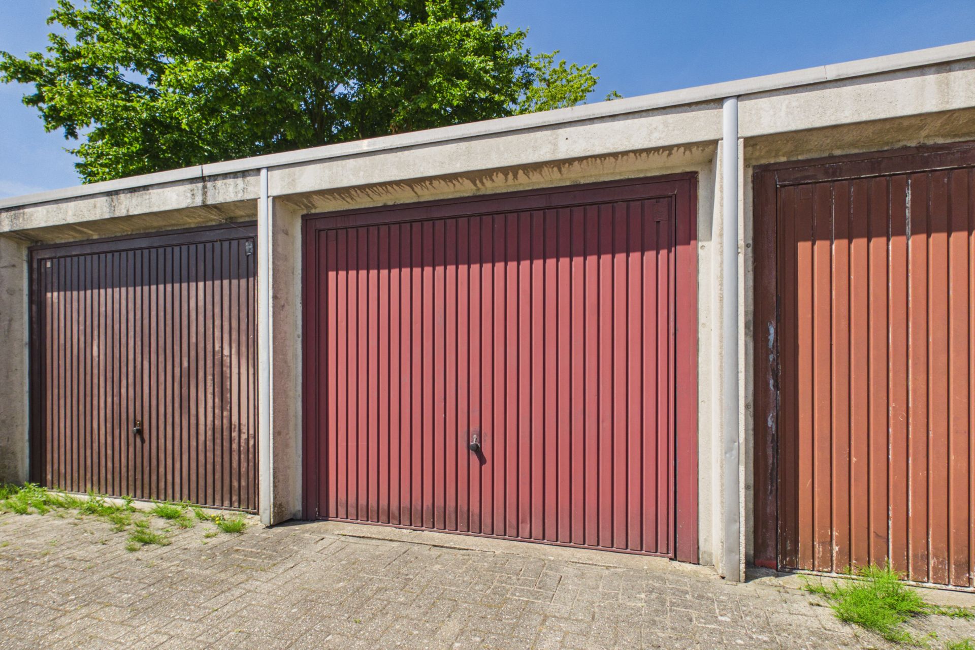 Drei nebeneinander stehende Garagentore aus Metall, davor gepflasterter Boden.