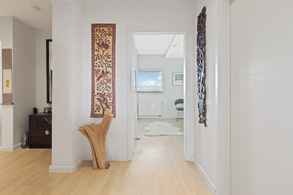Heller Flur mit Holzfußboden, Wanddekoration und Blick in ein Zimmer mit Fenster.