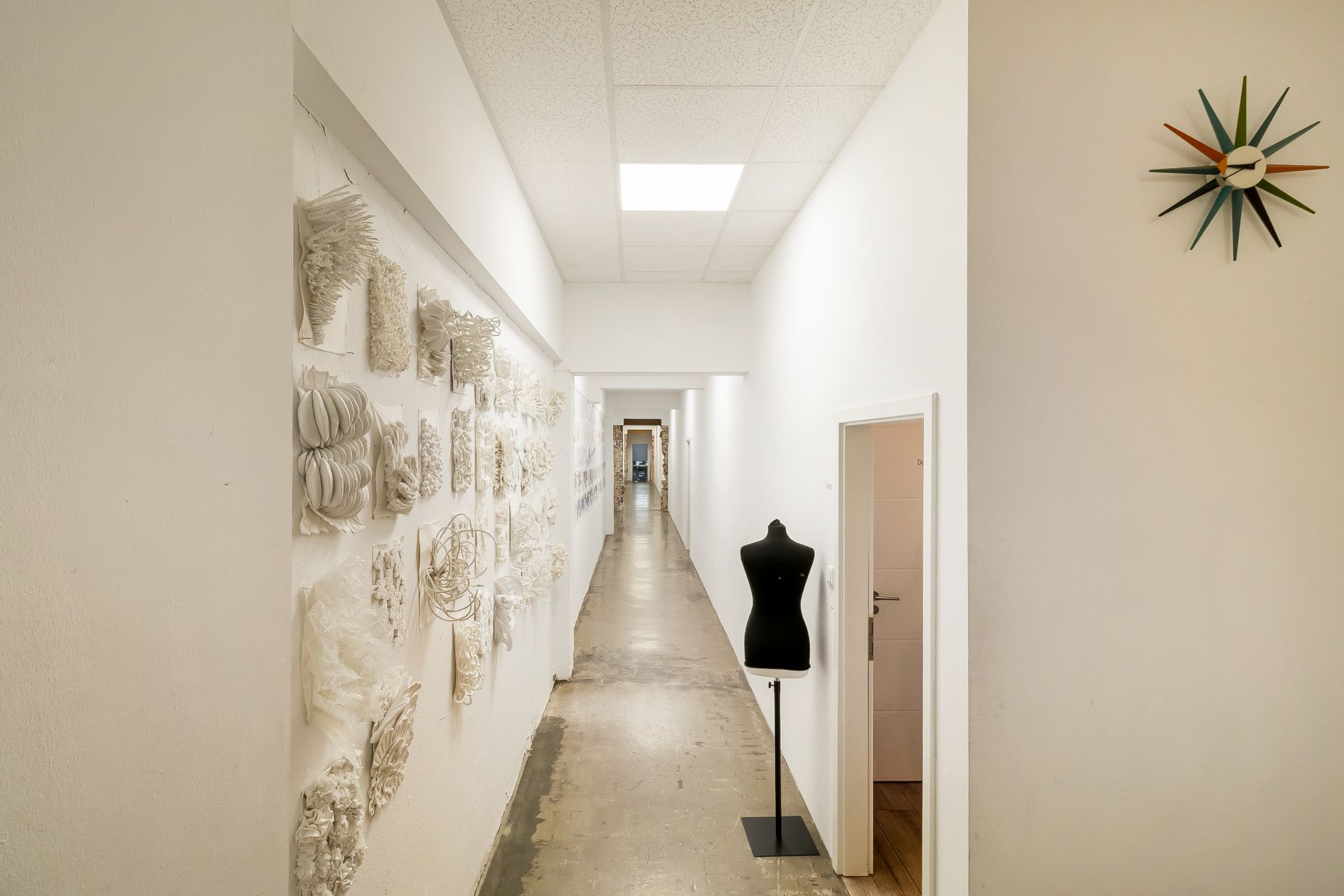 Langer Flur mit Kunst an der Wand, Schneiderpuppe und bunter Wanduhr.