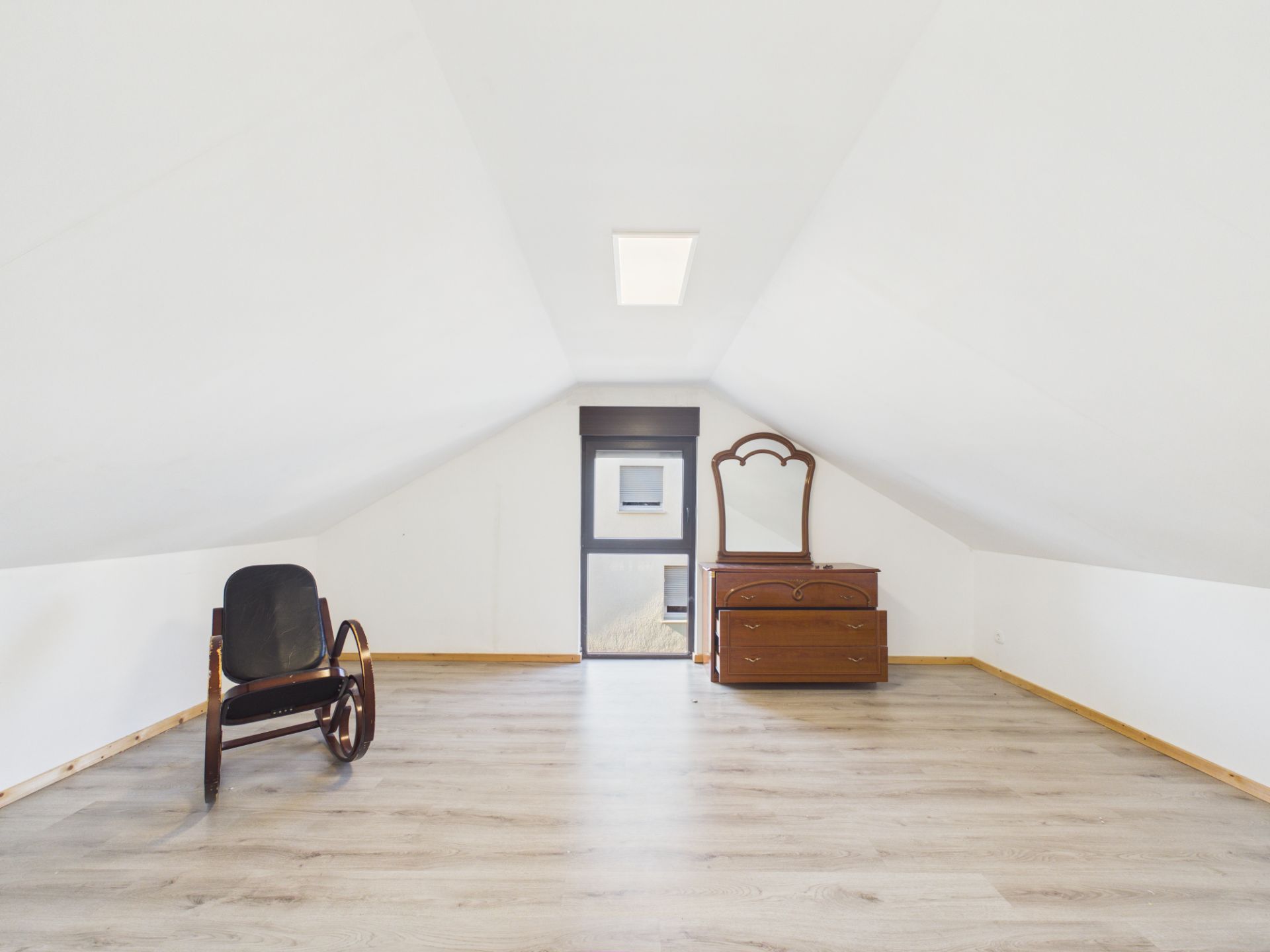 Dachgeschossraum mit Schaukelstuhl, Kommode mit Spiegel und Fenster.